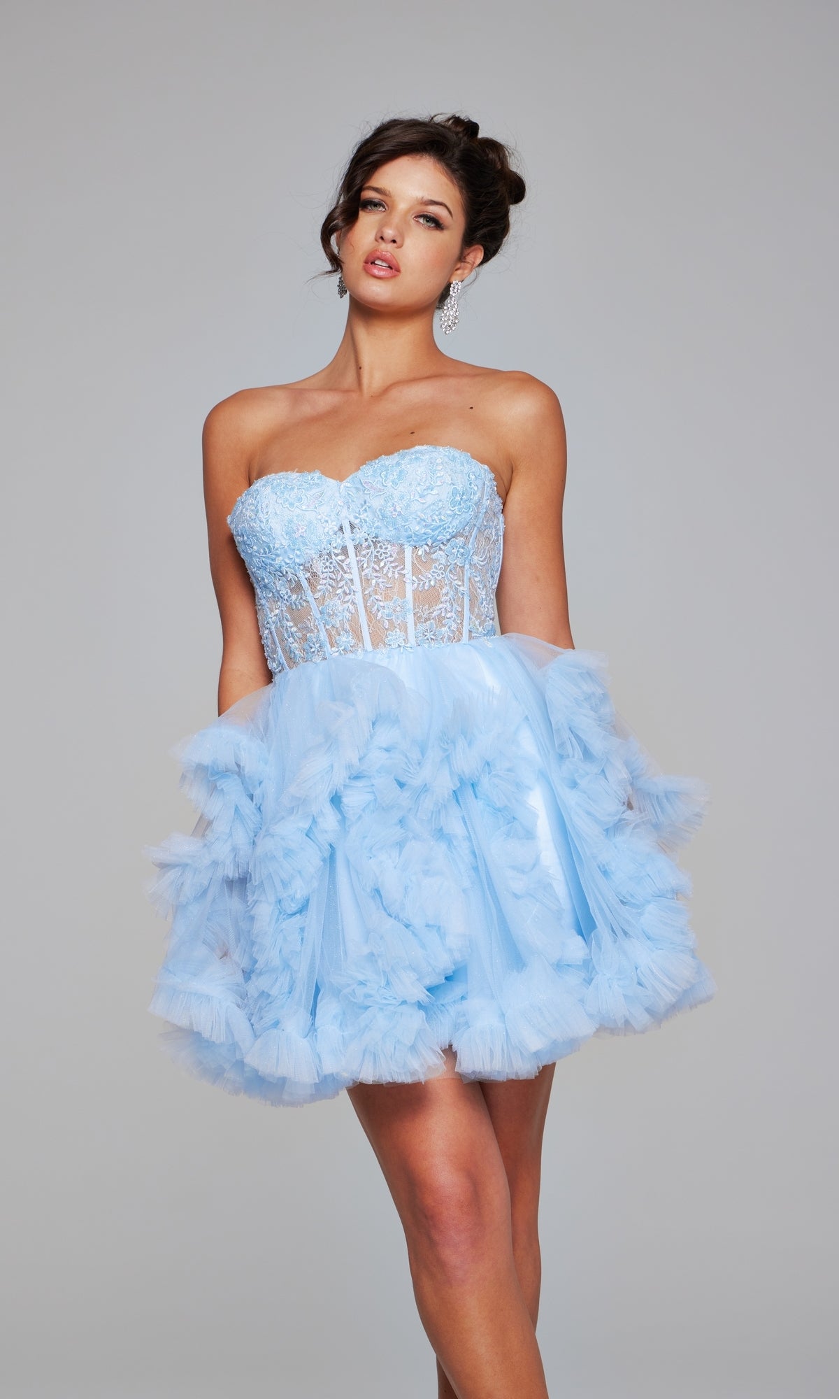 A woman stands against a plain gray background wearing the Short Homecoming Dress 40628 by Jovani, featuring a sweetheart neckline, sheer lace corset bodice, and a voluminous ruffled tulle skirt.